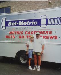 Founder Ralph with his mother, Bella, standing in front of a BelMetric delivery truck featuring a large bolt logo and text advertising “Metric Fasteners, Nuts, Bolts, Screws.”